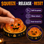 Hand pressing orange Halloween pumpkin squishy in black and gold display base